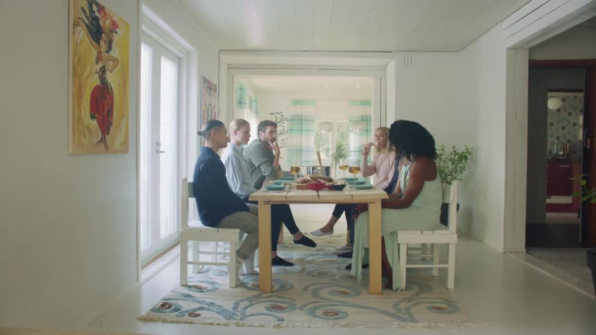 A group of friends sit around a dining room table talking and drinking wine