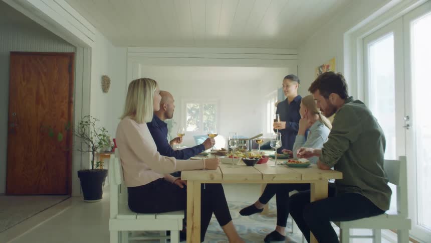 A person stands at a dinner table giving a toast to gathered friends