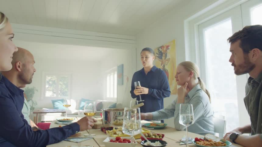 A woman stands at a home dinner table making a toast and holding a wine glass
