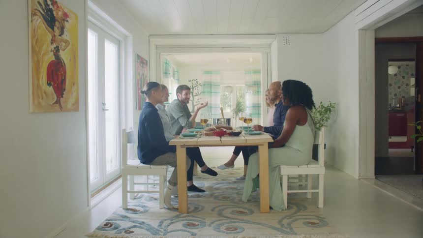 A group of friends sit around a table and talk during a meal in a home
