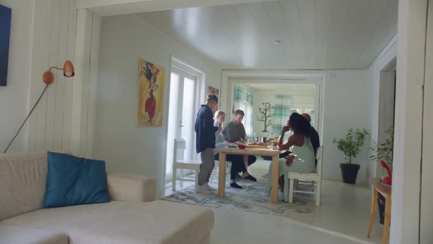 A group of people sit around a home dinner table and one person stands up