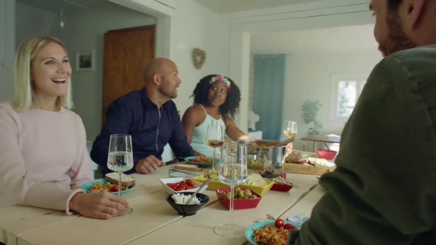 People sit around table with food and drinks talking and laughing