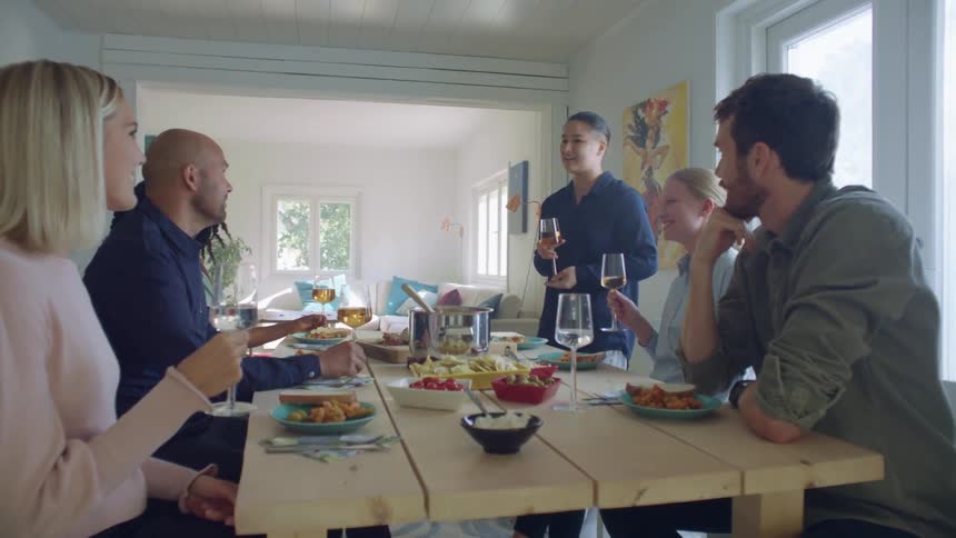 Friends talk and laugh over meal at dining table in home