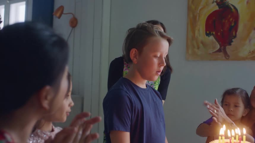 Boy blows out the candles on a birthday cake with his friends and family at home
