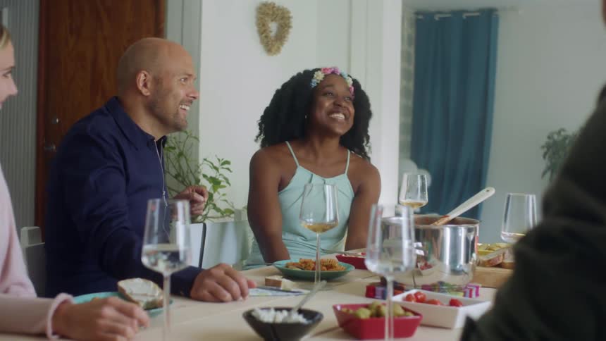 Men and women sitting at a table with food and drinks talking and smiling