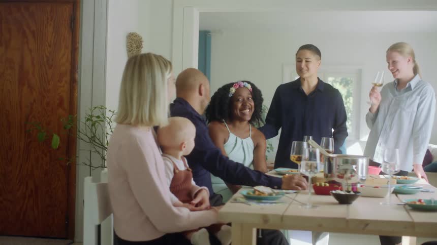 A group of men and women are talking after eating in a dining room as another woman holds her child