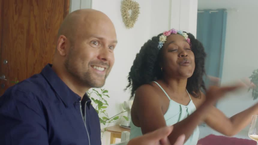 A group of people sit at a table in a home and talk at a table with wine