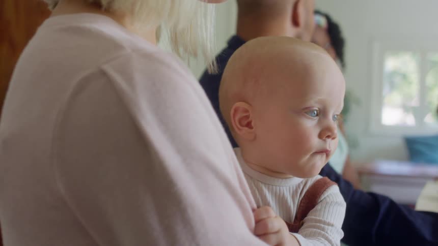 A woman holding a baby sits in a house and talks with other people