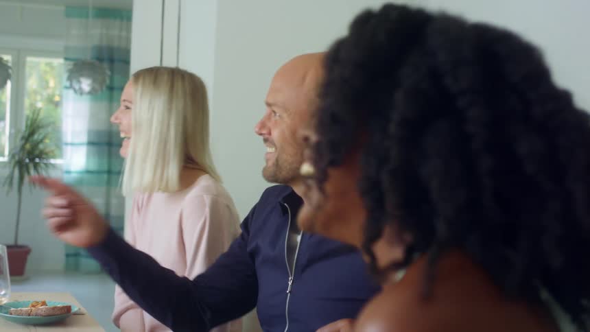 Group of friends sitting at the dinner table at home laughing and smiling
