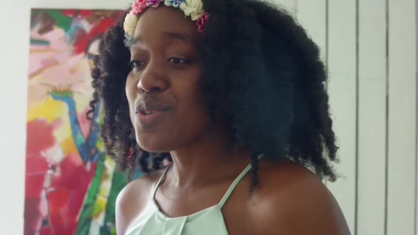 Girl with curly hair and a floral wreath talks to people in a room