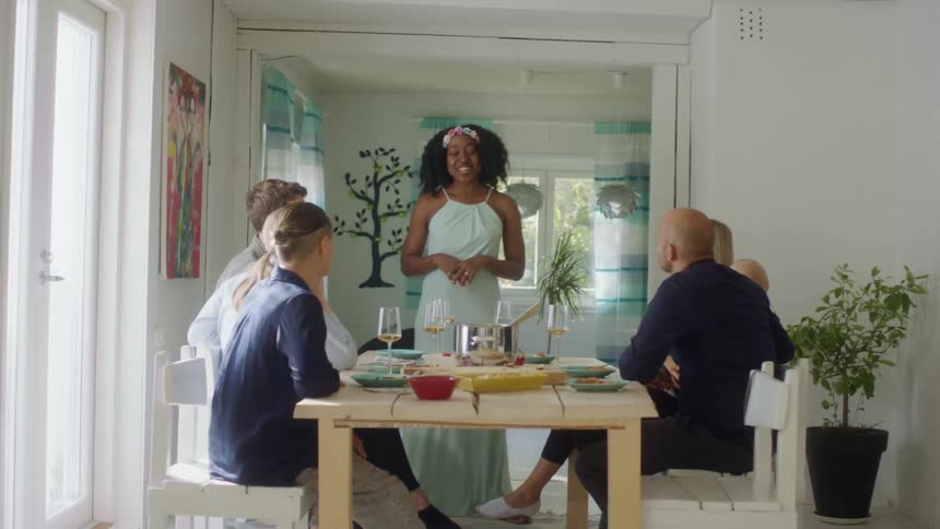 Woman standing in front of a dining room table talking to her friends sitting around the table