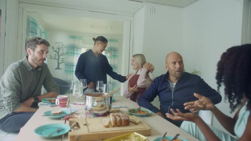 A group of people sit around a dining table talking together