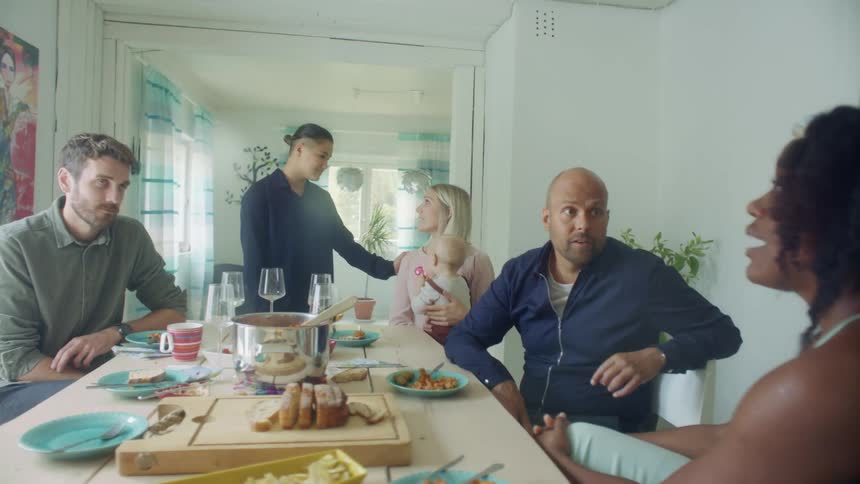 A group of people sit around a table with food and drinks and talk