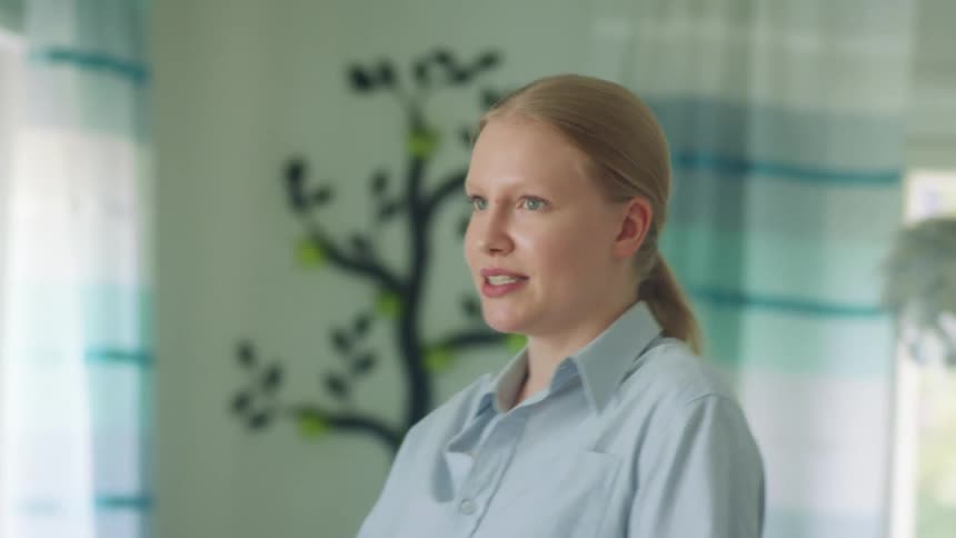 Blonde woman with a ponytail and a light blue shirt talks to people in a room