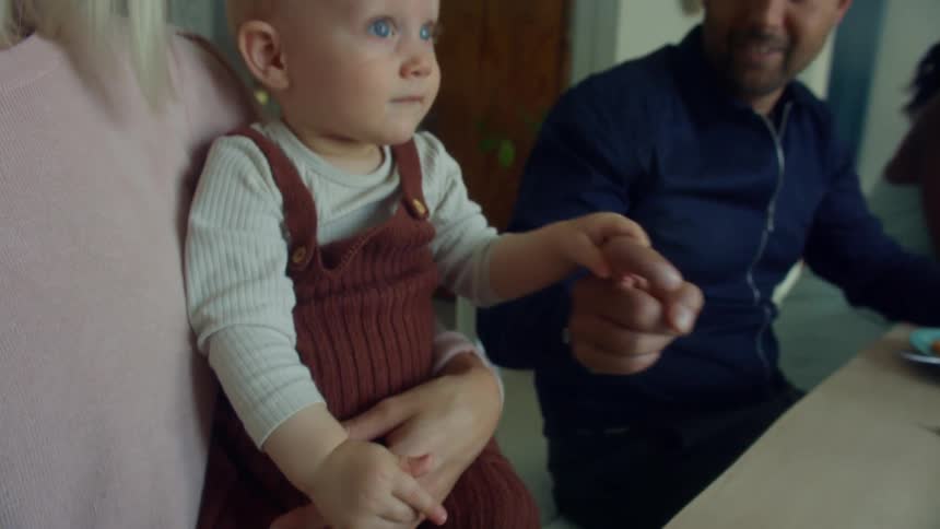People sit at a table talking and smiling a dad holds his daughter hand while the mother holds the baby