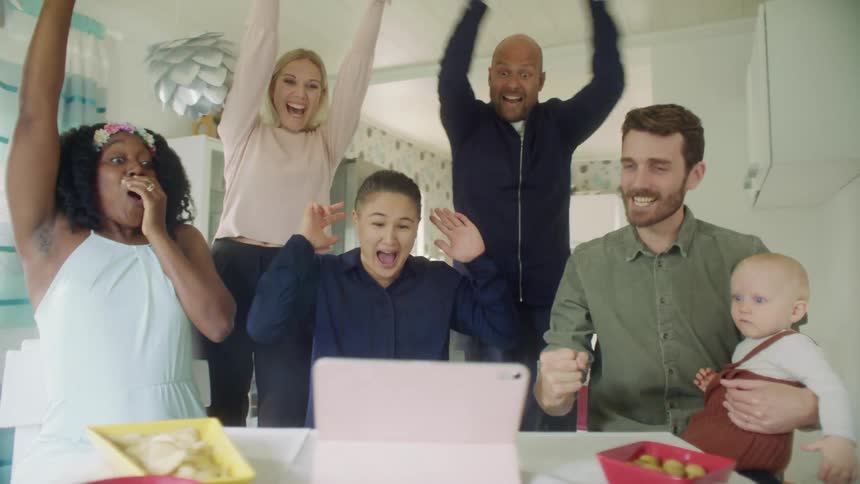 People sit cheering something that happened on a tablet with snacks on the table