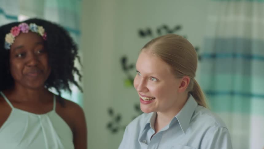Two women laughing and smiling amongst each other with other friends inside of a home