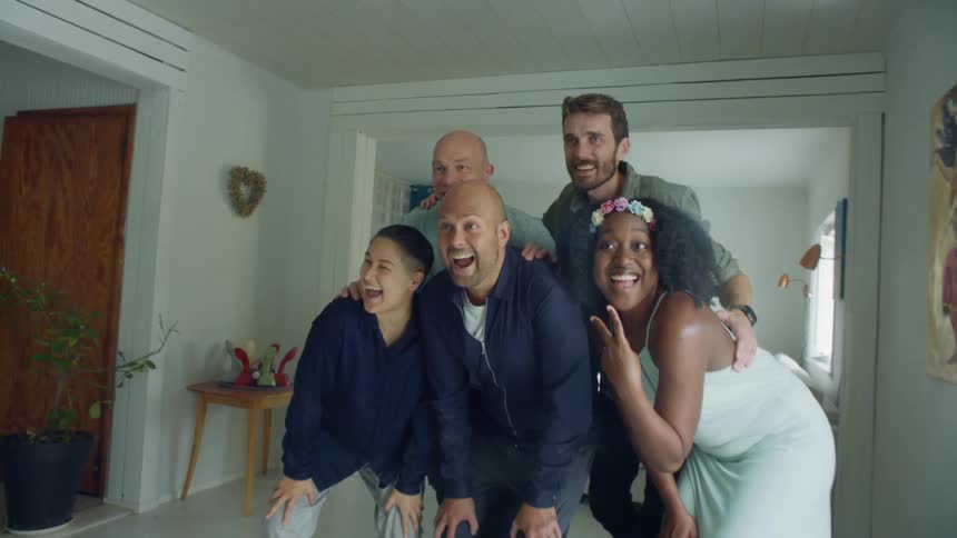 A woman uses her smartphone to take a picture of her friends posing in a house