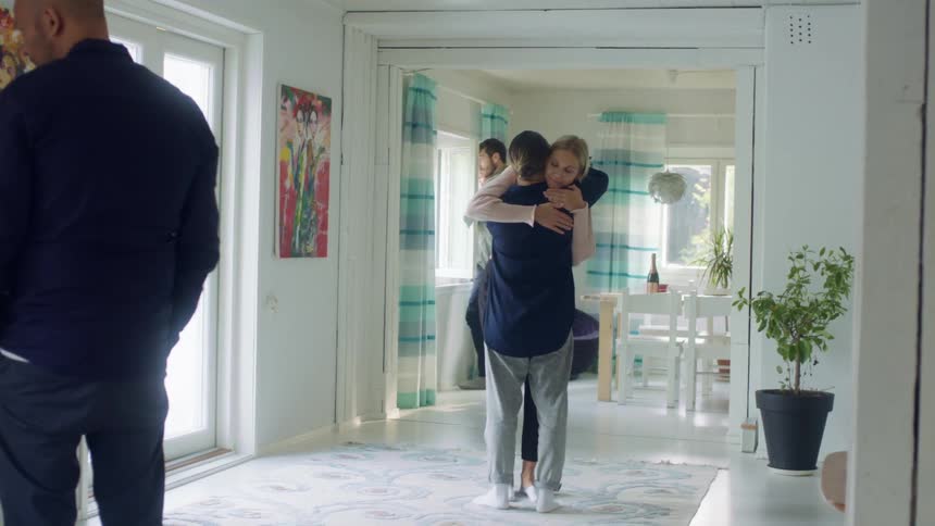 Two women in a house walk towards one another and hug