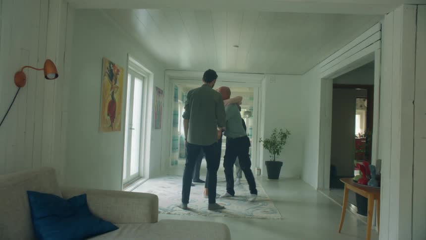 A man walks in to a home and shakes a mans hand and hugs a woman and gives her a bottle of wine