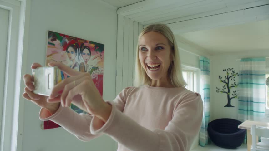 A woman laughs and talks as she takes a photo at home with her cellphone