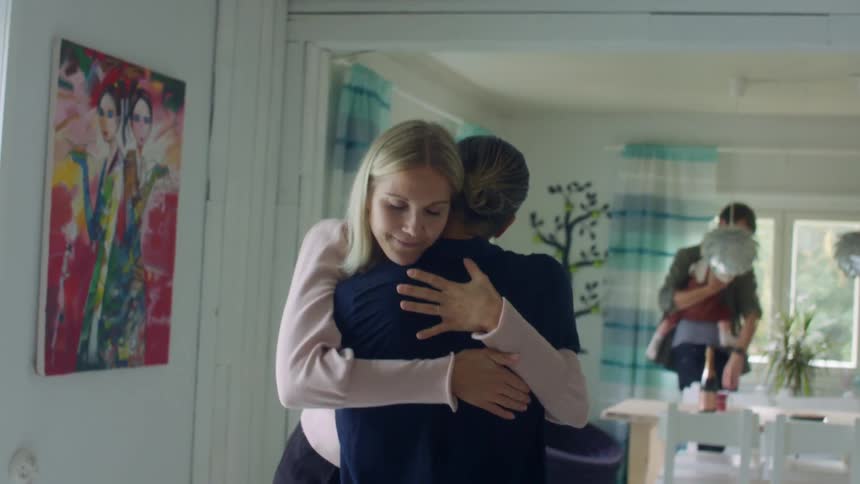 A father holds his baby at home as two women hug