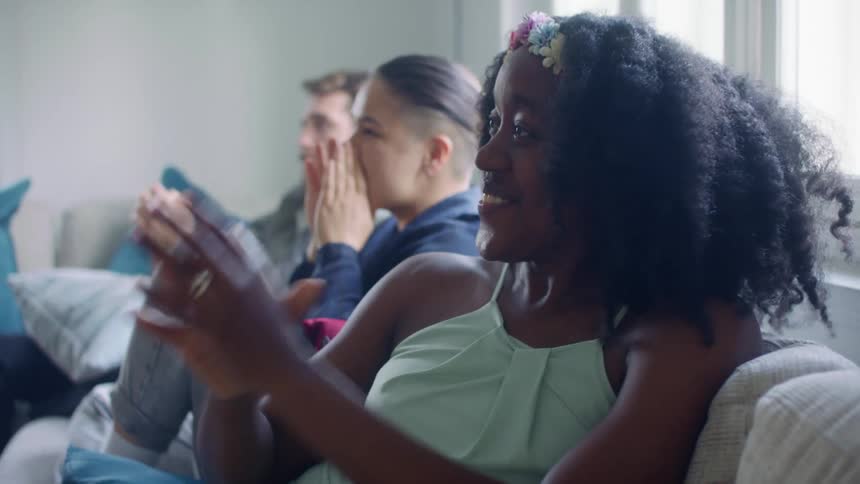 A man and two women sit on the couch happily clapping together