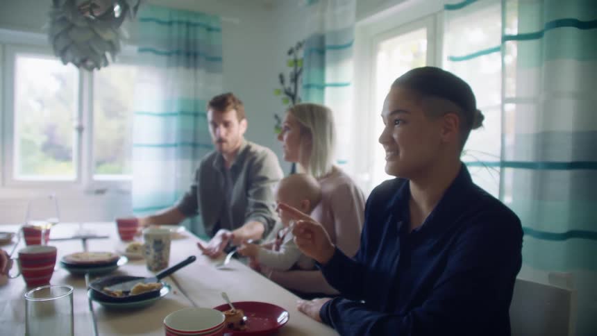 A group of people and a baby sit at a dining room table after a meal talking and laughing