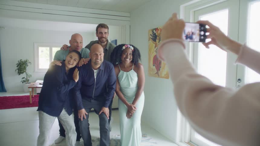 A group of people pose while am woman takes pictures of them on her cell phone