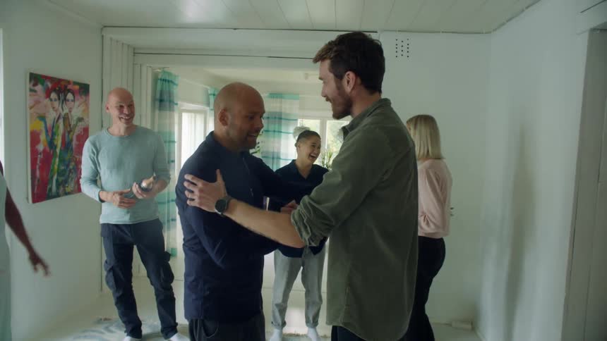 A group of people talking and laughing indoors are greeted by a man