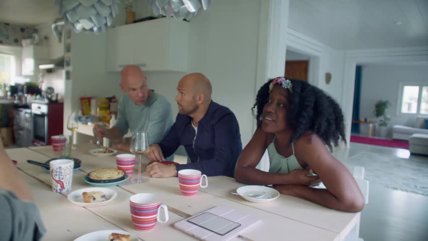 A woman sitting at the end of a dining table in a house talks with a man sitting across from her