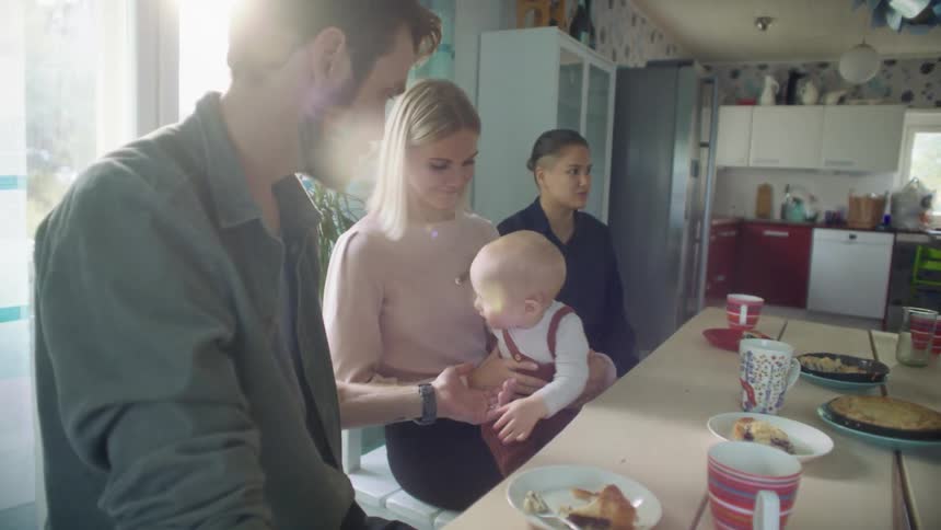 A man holds his hand out for the spoon being held by the baby sitting in the lap of a woman sitting next to him at a dining table