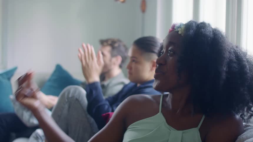 Three people sit on a couch indoors and clap their hands and dance