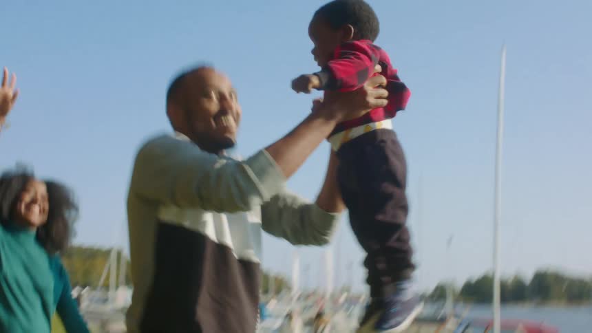 A man tosses a small toddler up in the air standing beside a marina