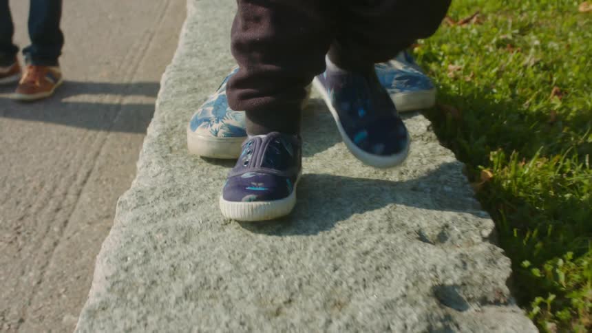 Older adult helps young child toddle across concrete border of yard