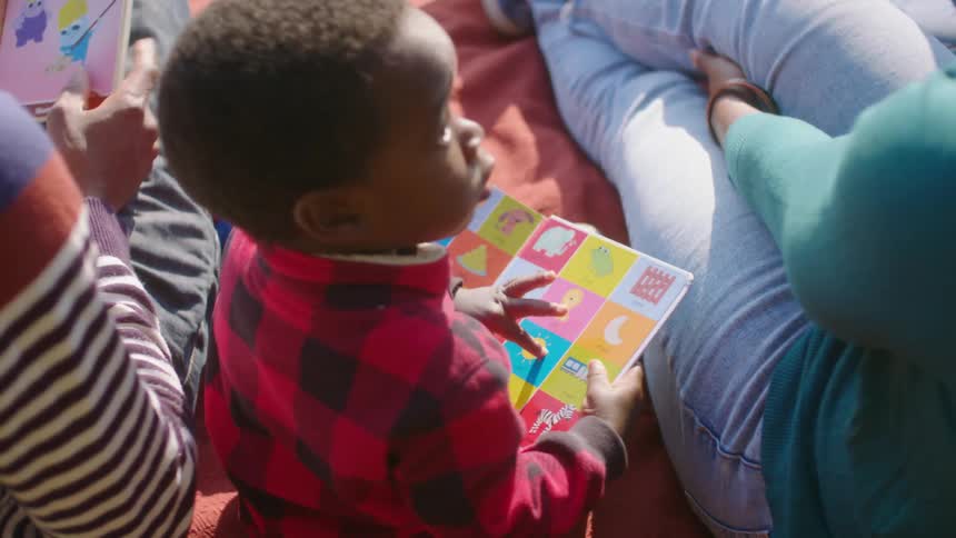 A little boy sitting outside next to his mother looks at pictures and looks up at her