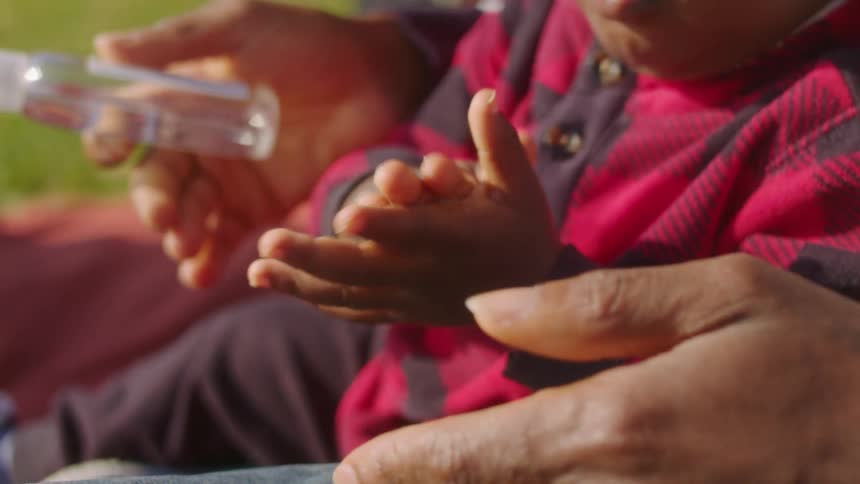 A man pours hand sanitizer into the hand of a small boy and helps him to rub his hands together