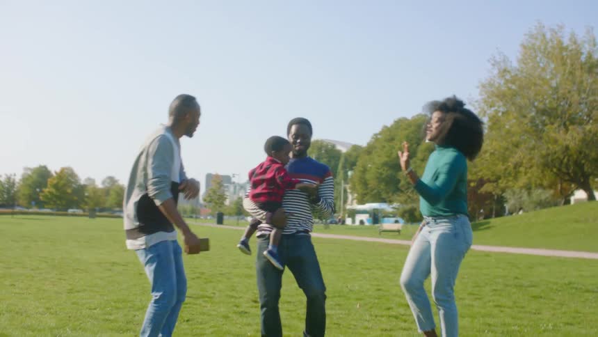 A man and woman dance with their infant and another man in a public park