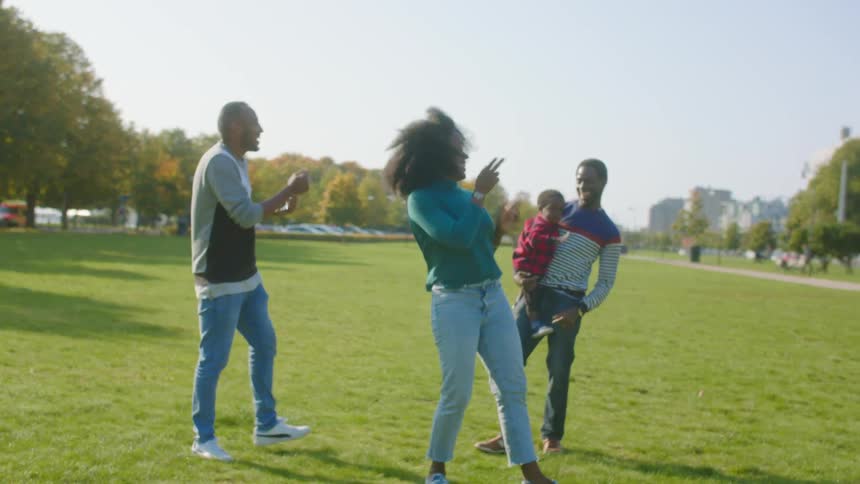 A man holding his young son dances in a public park with a woman and another man