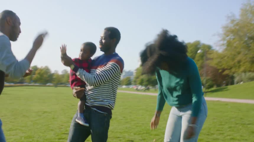 A man holds a boy while he stands next to a man and woman dancing outdoors in a park during the day