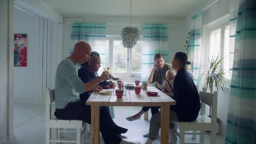 A group of people eat and drink while they talk at a dining table in a small home dining room