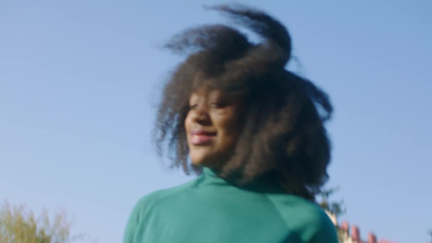 Black girl with a turquoise blue turtleneck sweater and a boy dance on the grass in the public park