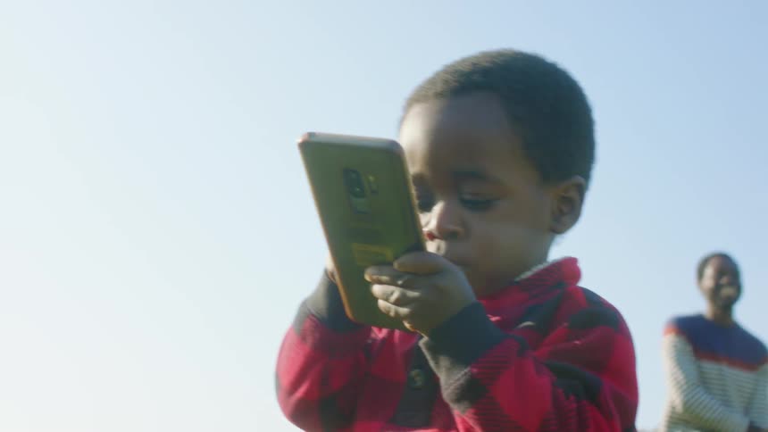 Three people dance in a public park as a little boy plays with a cell phone