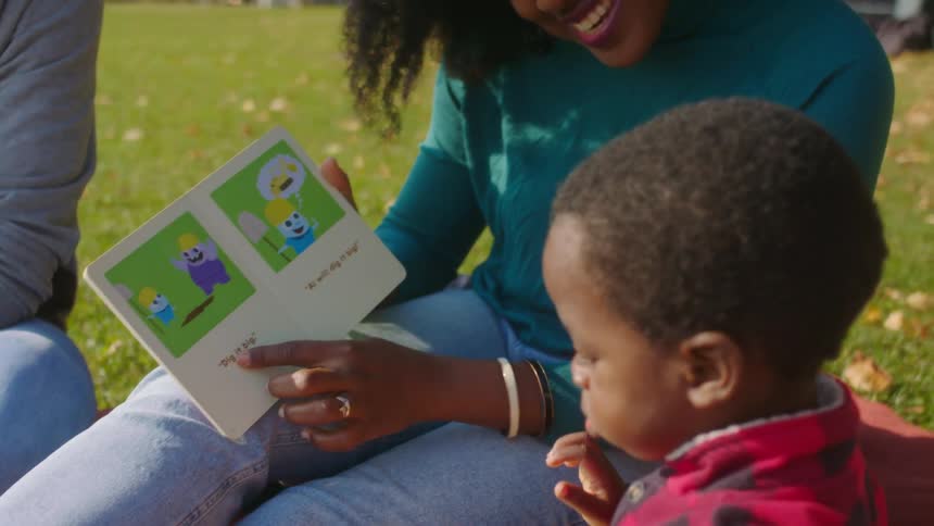 Mother showing her son a story book sitting on the grass in a park
