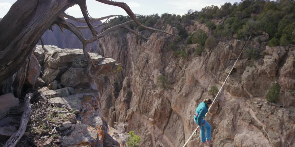 A woman is sitting on a tightrope over a large drop