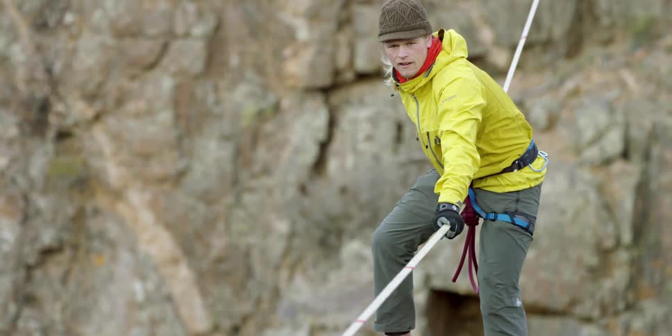 A person balances themselves on a rope between two large rock formations