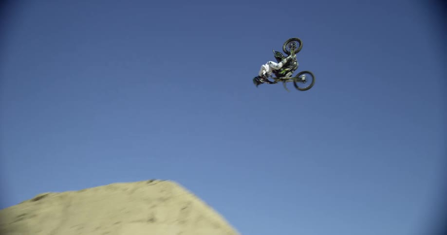 Man rides a motorcross motorcycle over a sand ramp for a big acrobatic jump
