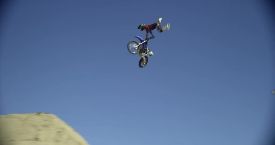 A person at a motocross track goes over a jump and kicks their legs back behind the bike