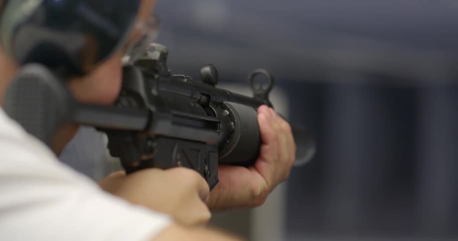 A man holds a rifle in order to aim it at a target indoors
