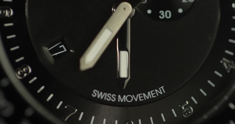 A watch with swiss movement has a black face with white text and tick marks